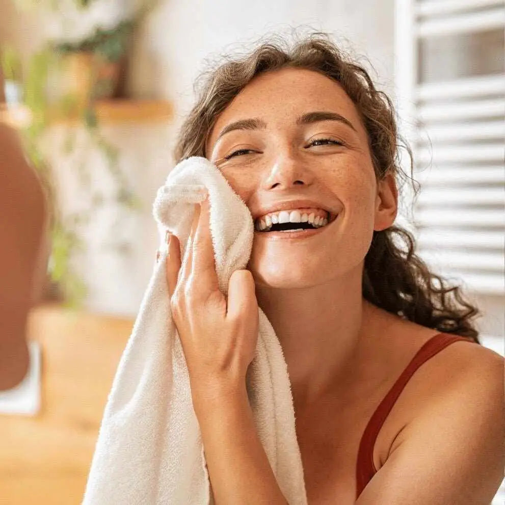Donna sorridente asciuga viso con morbido asciugamano bianco