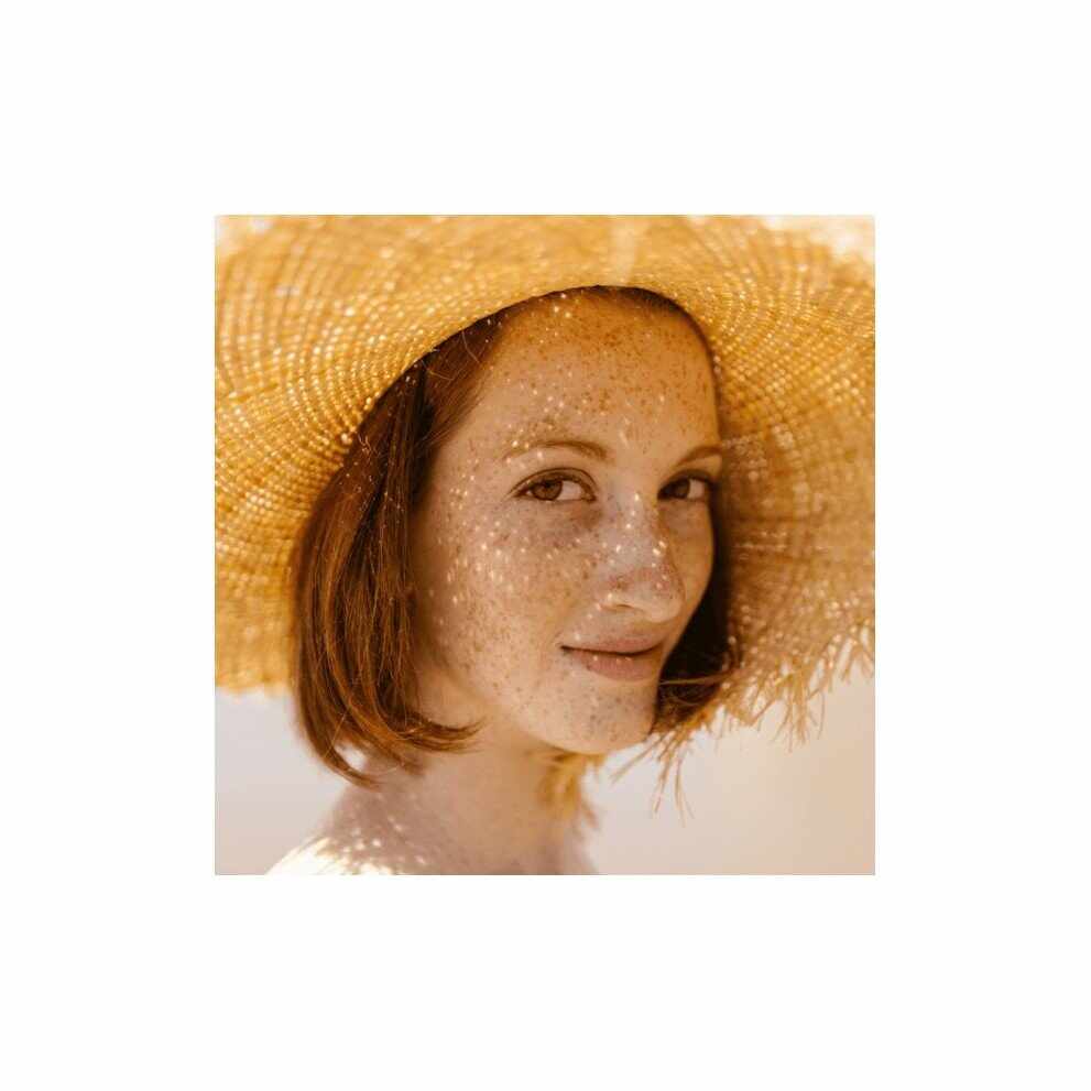 Donna con lentiggini e cappello di paglia per cura capelli estivi