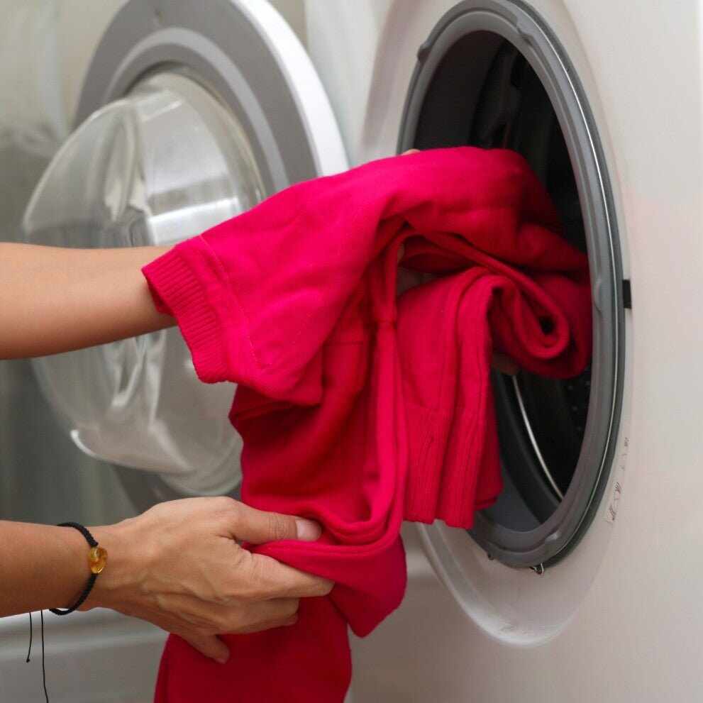 Persona che carica un capo rosso nella lavatrice frontale