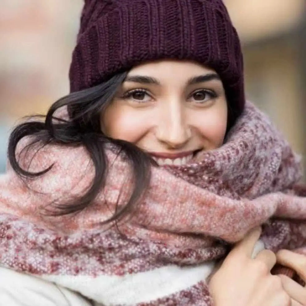 Giovane donna con cappello viola e sciarpa rosa che sorride al freddo