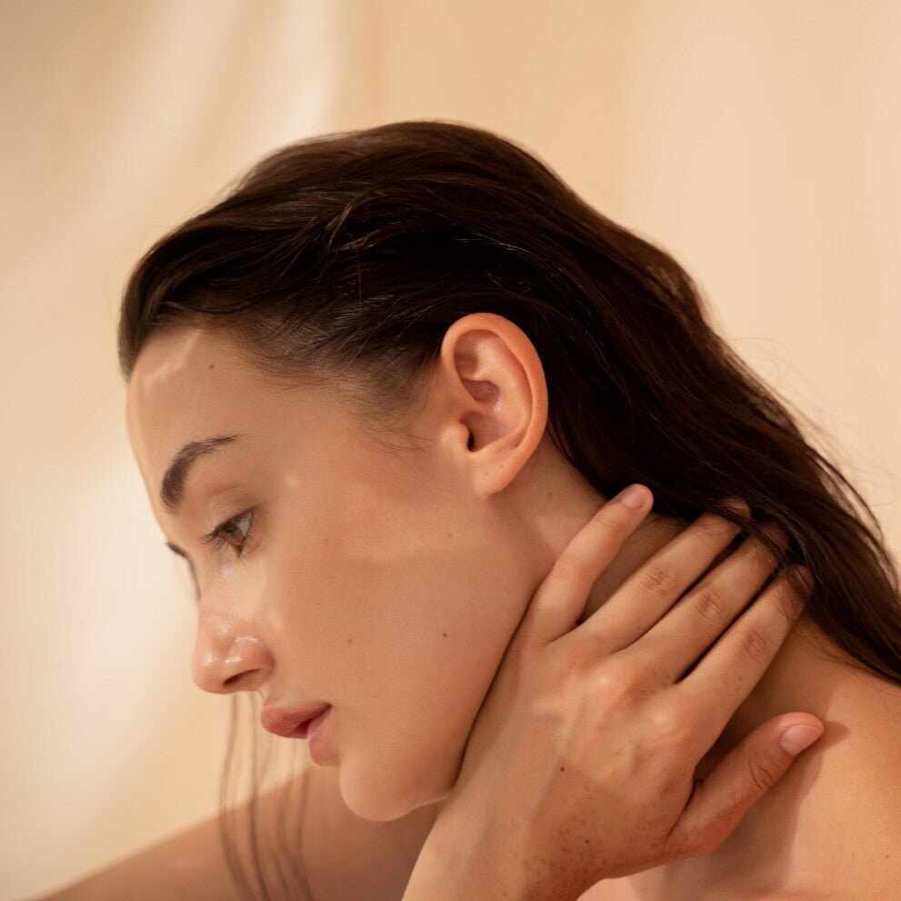 Donna con pelle chiara e luminosa, mano che tocca il collo