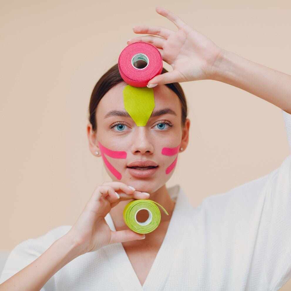 Donna con nastro kinesio colorato sul viso che tiene rotoli di tape
