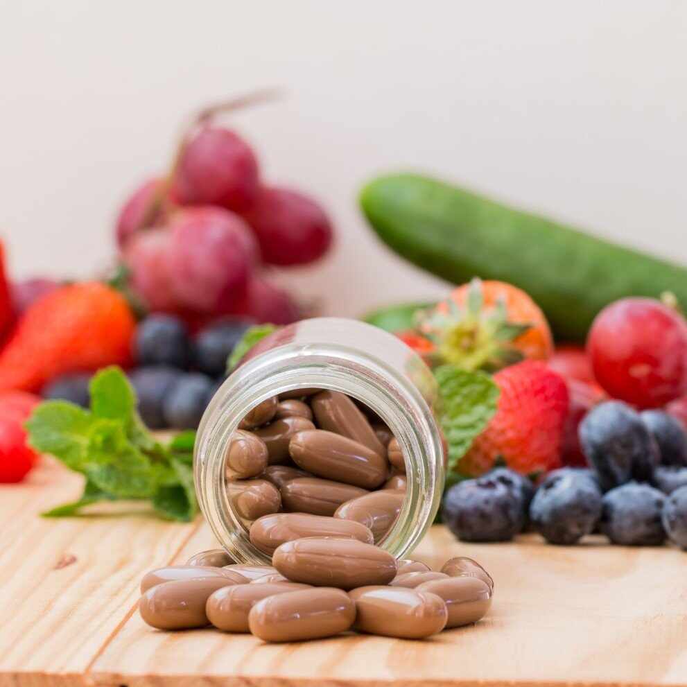 Barattolo rovesciato di capsule vitaminiche marroni tra frutta e verdura fresca