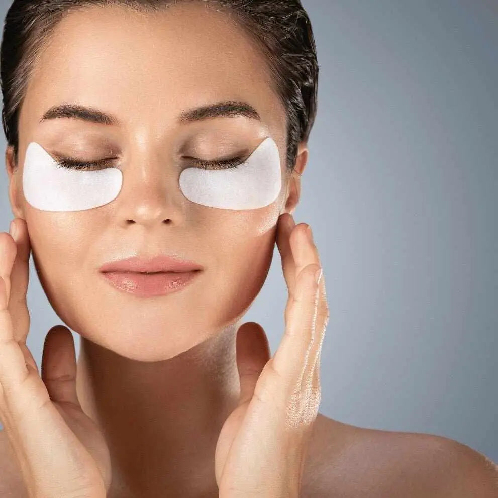 Donna con occhi chiusi indossa patch sotto occhi e tocca viso nella routine serale