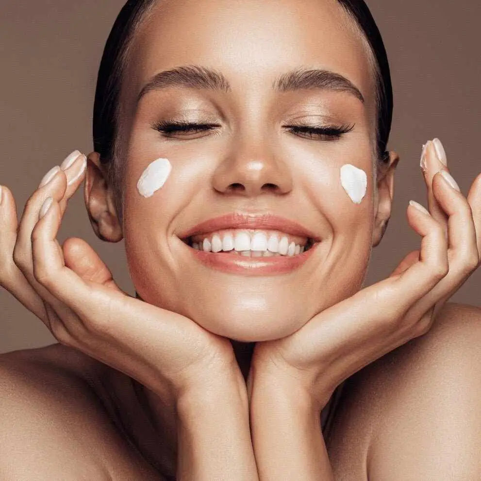 Donna sorridente applica crema bianca sul viso nella routine skincare