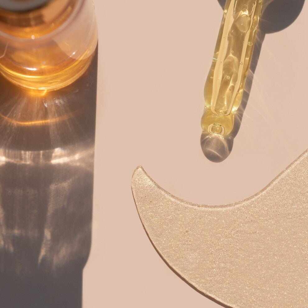 Pipetta cosmetica con niacinamide dorata su patch occhi a mezzaluna