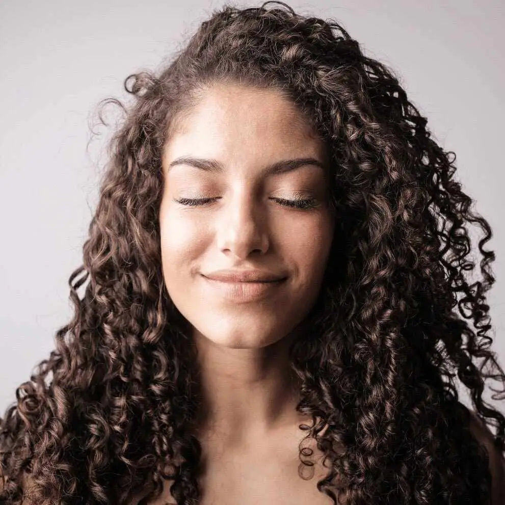 Giovane donna con capelli ricci idratati sorride a occhi chiusi