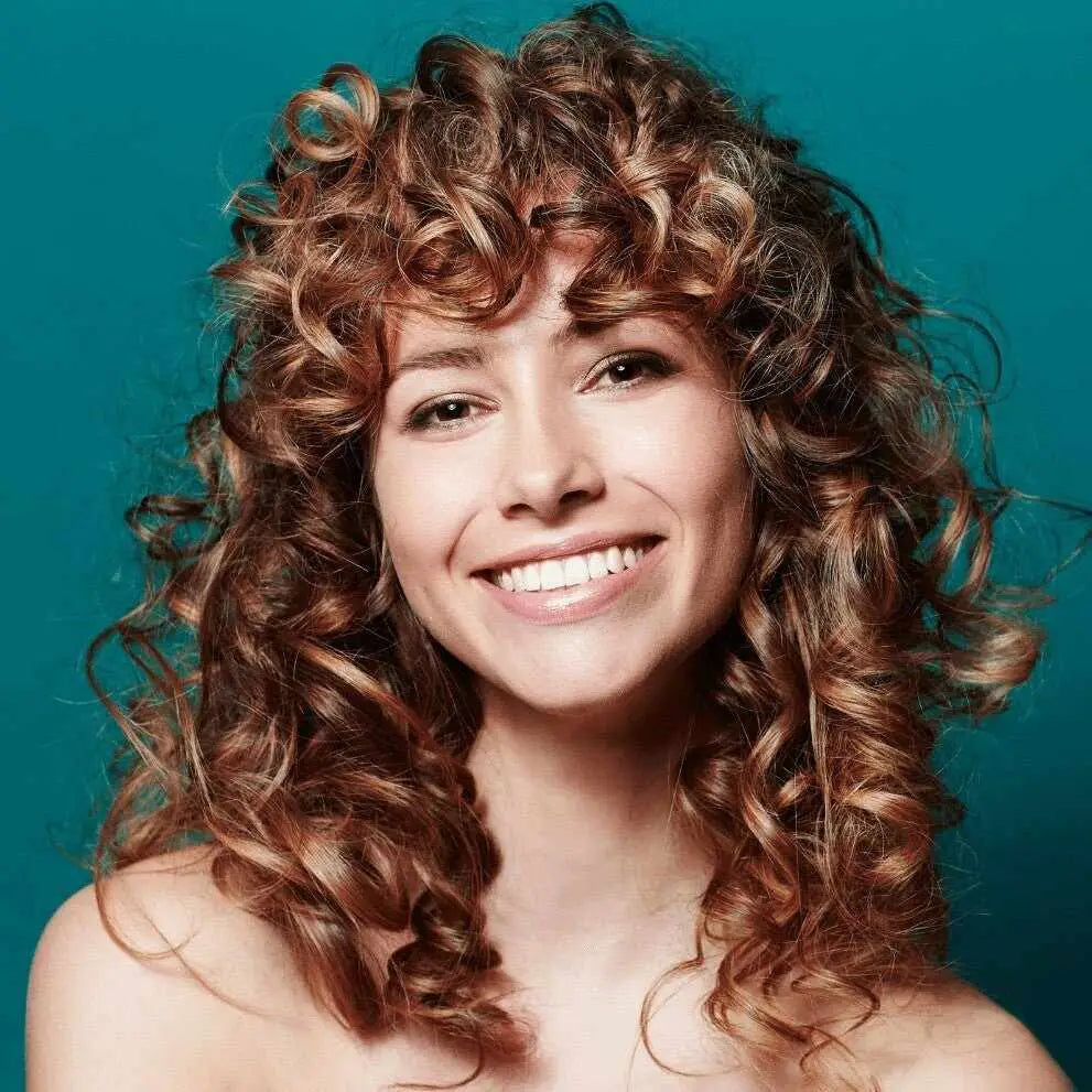 Donna sorridente con capelli ricci castani a spalla e frangia