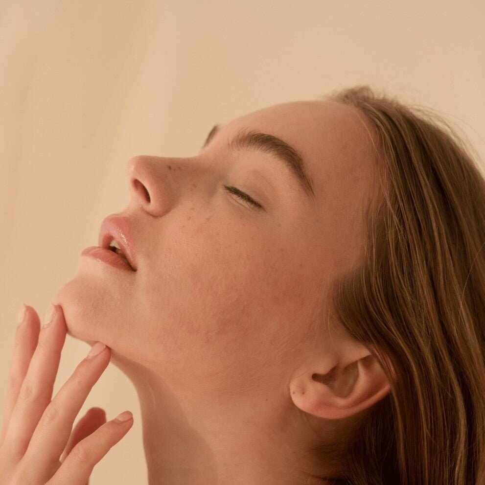 Giovane donna con occhi chiusi tocca il mento per reset pelle post-estate