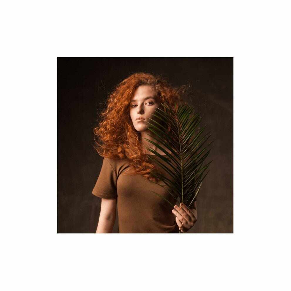 Donna rossa con maglietta marrone e fronda di palma verde per il Curly Girl Method