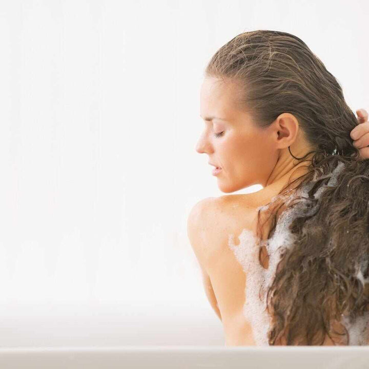 Donna con lunghi capelli scuri schiumosi in vasca da bagno