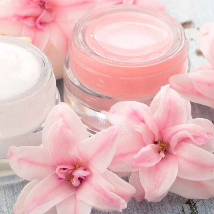 Creme cosmetiche rosa e bianche in vasi di vetro con fiori rosa, PAO e conservazione