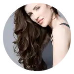 Una donna con capelli lunghi e mossi, di colore marrone scuro, che indossa un top scuro.