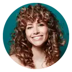 Una donna sorridente con capelli ricci voluminosi di media lunghezza e castani.